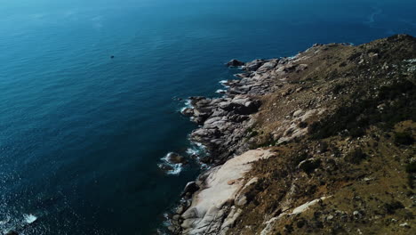 Stones-near-blue-ocean-water-on-majestic-Vietnamese-coastline-in-Ninh-Thuan,-aerial-fly-backward-view