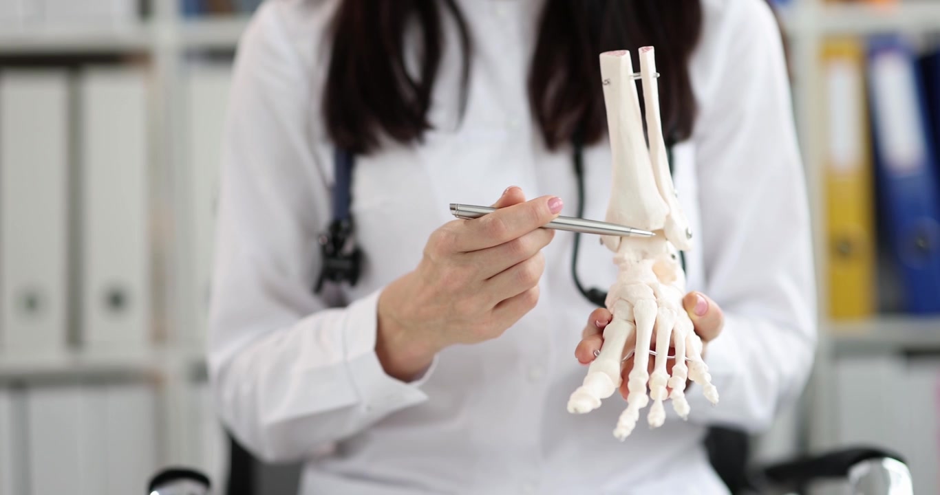 Doctora muestra modelo de articulación de tobillo humano en consultorio médico