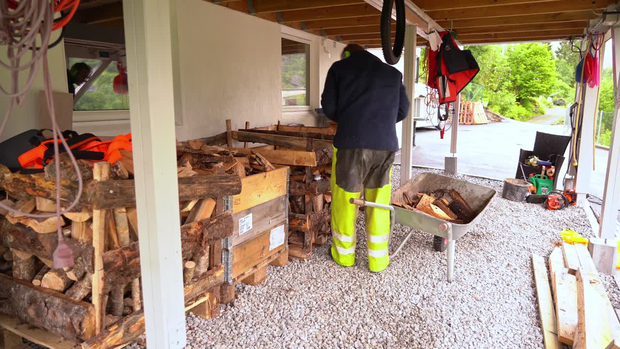 Man som står under sin balkong och kastar nyhuggen ved i lådor för torkning och förvaring inför vintern.