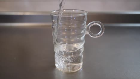 Full-shot-of-water-being-poured-into-a-glass-cup-on-a-metallic-kitchen-worktop,-health-and-clean-water-concept,-slow-motion-footage