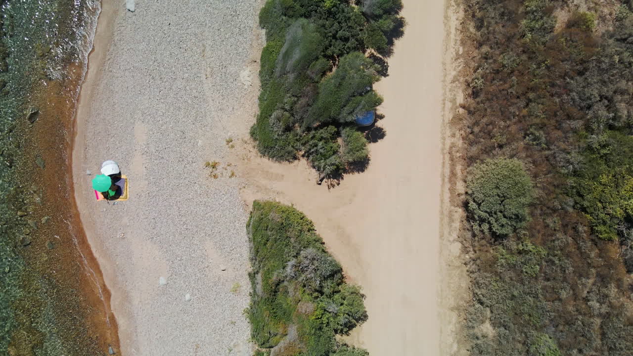 vista de pájaro de la playa idílica con turistas bajo el paraguas en la orilla del mar durante un día cálido y soleado en cerdeña, italia - toma aérea de drones