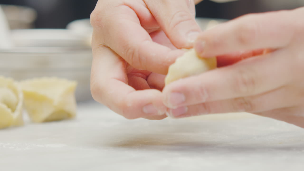Close-up of a chef's hands forming a handcrafted ravioli with artistic detail, accompanied by molds and more pieces out of focus in the background