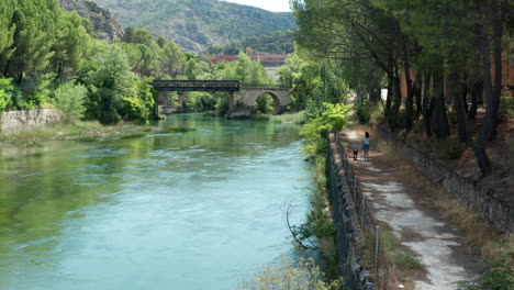 Follow-shot-of-young-woman-walking-her-pet-dog-along-the-riverbanks