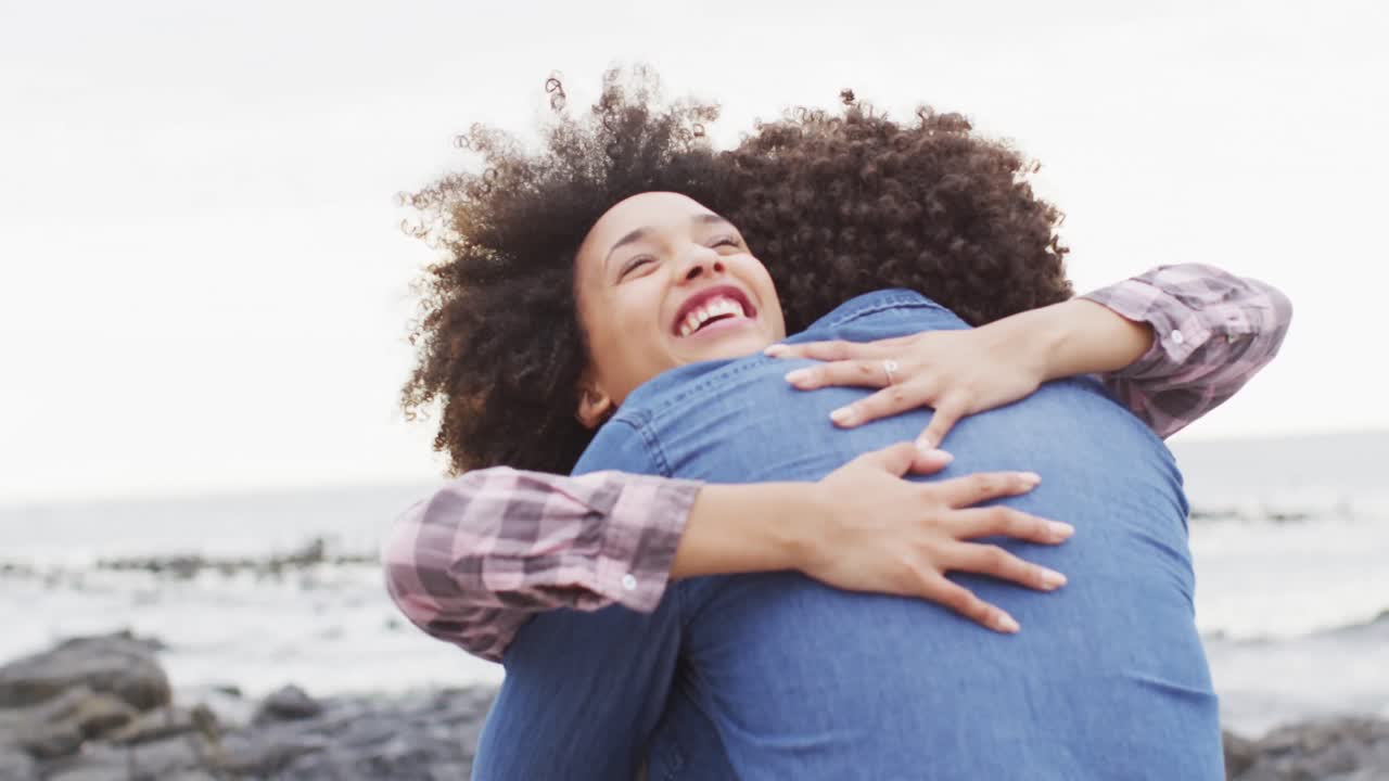 mujer afroamericana abrazando a su marido en las rocas cerca del mar