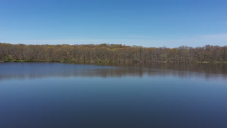 Luftaufnahme-Eines-Blauen,-Spiegelnden-Sees-Mit-Kahlen-Bäumen-Am-Seeufer