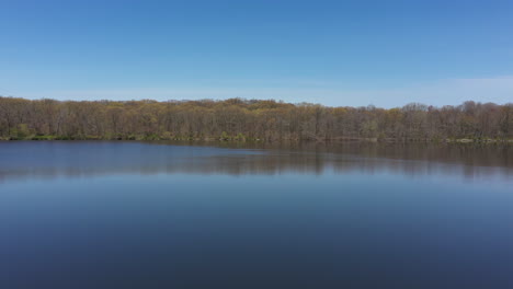 Una-Vista-Aérea-De-Un-Lago-Azul-Reflectante-Con-árboles-Desnudos-Que-Bordean-El-Borde-Del-Lago