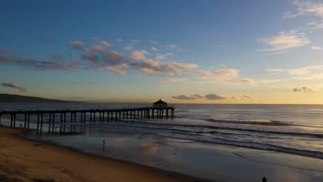 aerial view of manhattan beach pier, california, with waves crashing on the sandy shoreline, at sunset