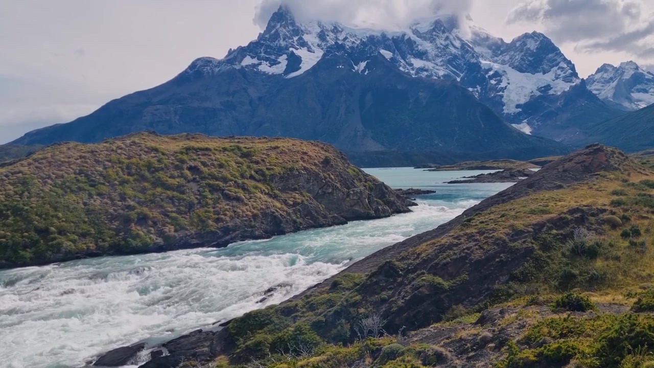 Fiume che scorre dal Lago Nordenskjöld verso Salto Grande e il Lago Pehoé, incorniciato dalle cime innevate delle Torres del Paine in Cile, che mostra la natura selvaggia incontaminata e la drammatica natura patagonica.