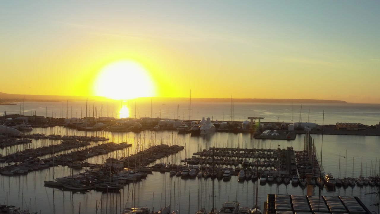 Drone avança sobre iates na marina de Palma enquanto o pôr do sol brilha sobre Maiorca, Espanha