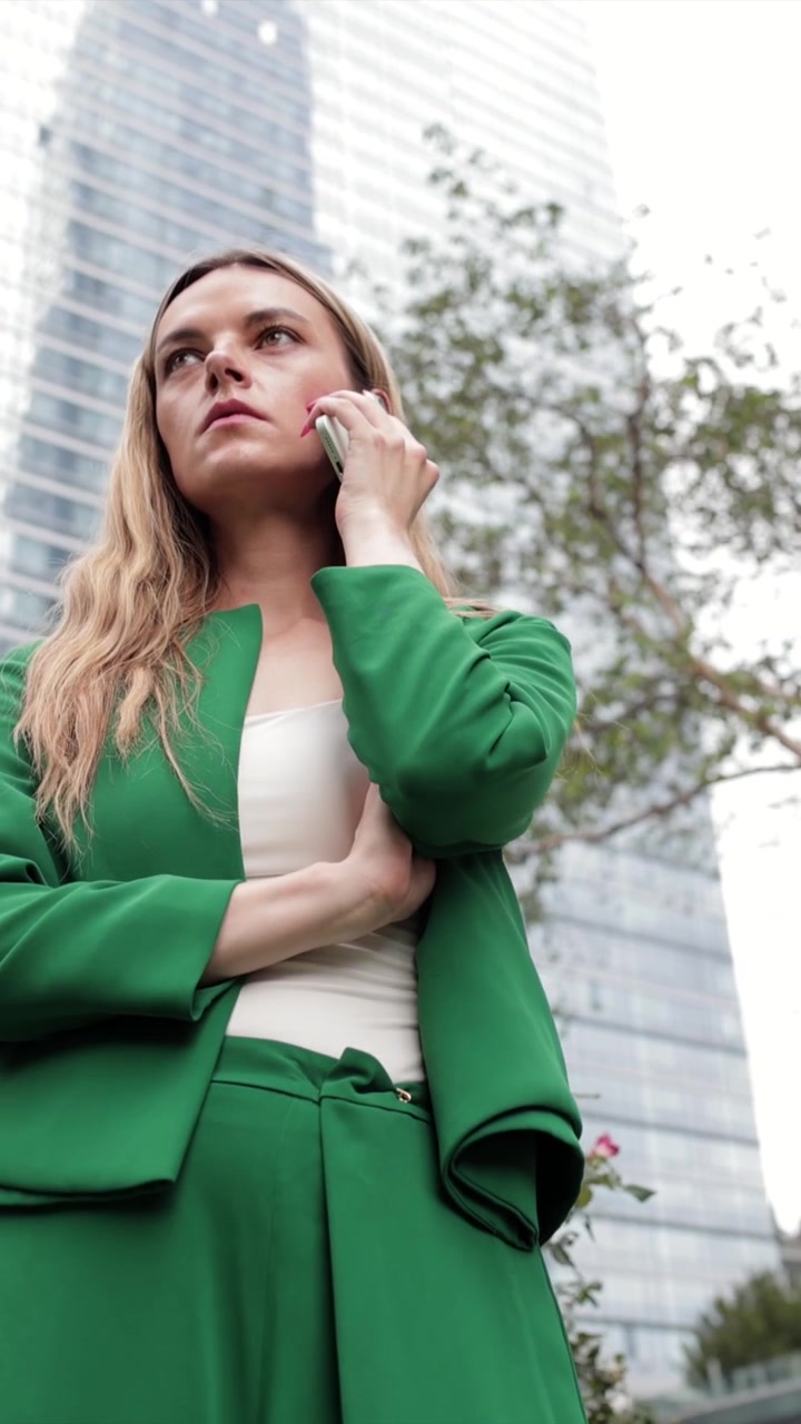 Empresária de terno verde falando ao smartphone na cidade
