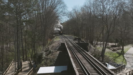 Aerial-drone-shot-of-a-steam-train-engine-moving-down-the-tracks-in-Chattanooga,-TN