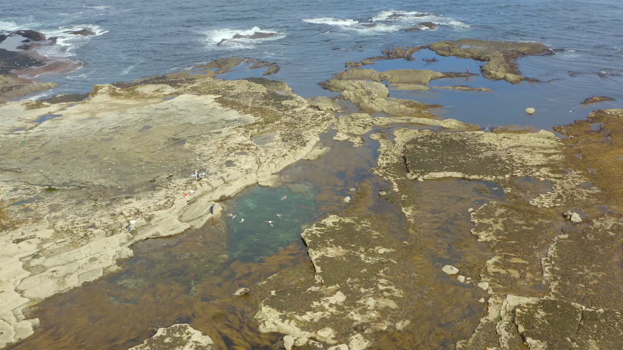 Dynamic aerial shot zooming in on a tidal pool in Kilkee, Ireland, featuring swimmers. Slow motion