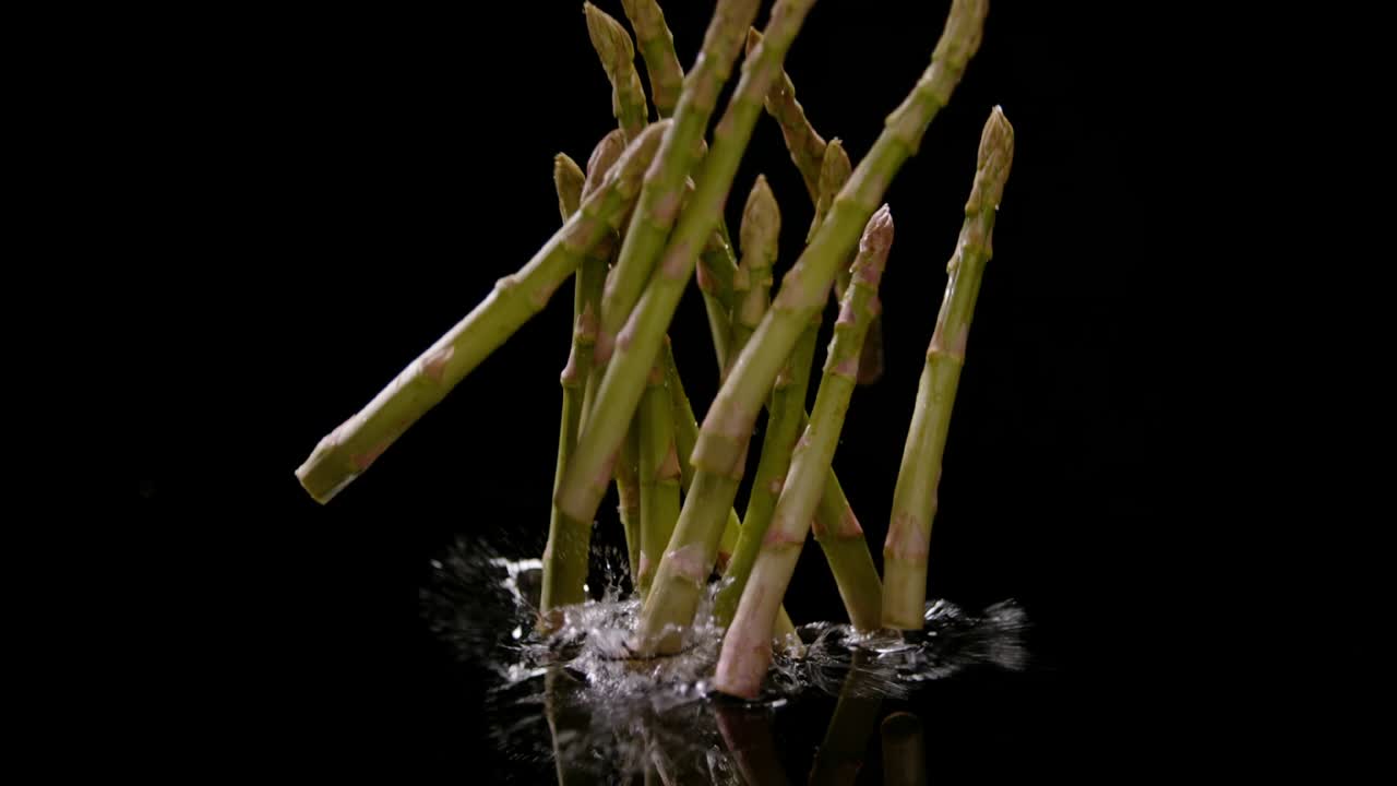 Bunch of asparagus fall into water isolated on black background, ultra slow motion