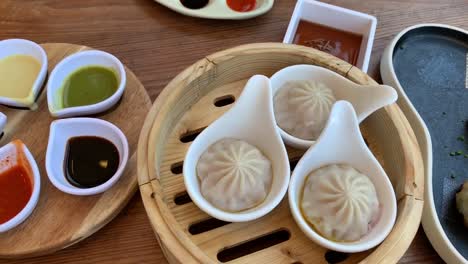 chinese dimsum neatly plated on a wooden table with a colorful array of dipping sauces