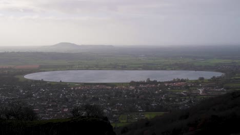 English-rural-countryside-village-of-Cheddar-in-Somerset,-with-a-view-from-Cheddar-Gorge-of-large-water-reservoir-on-a-overcast,-grey-and-misty-day