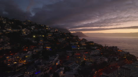 Forwards-fly-above-residential-buildings-in-town.-Aerial-view-of-sea-coast-at-sunset.-Cape-Town,-South-Africa