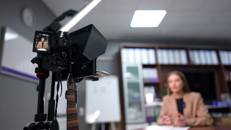 display of camera on tripod shows a brunette woman in beige jacket. low angle view. blog creation in the office.