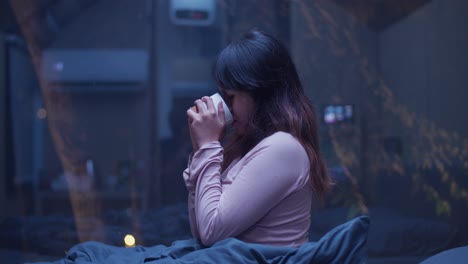 indonesian girl drinking tea at night in her room. view through the window