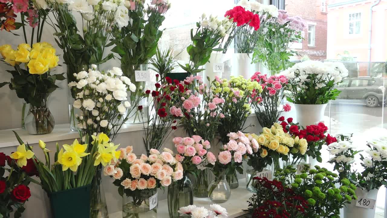 Helle Auswahl frischer Blumen, arrangiert in Glasvasen in einem Blumenladen. Rosen, Nelken, Narzissen und Chrysanthemen bilden eine lebendige Marktauslage im Innenbereich.