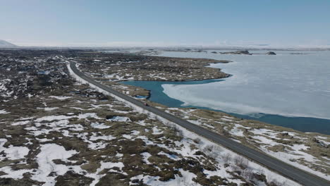 aerial view of car moving on road by frozen lake in landscape of iceland on sunny late winter day