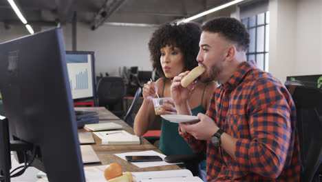 hombres y mujeres felices y diversos colegas comiendo en el escritorio y viendo la computadora en la oficina, en cámara lenta