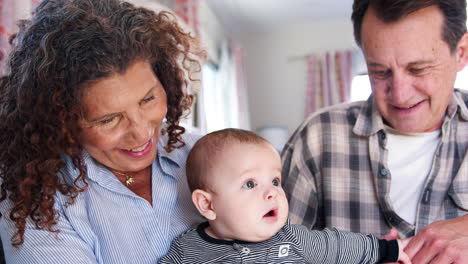 Grandparents-Sitting-On-Sofa-Playing-With-Baby-Grandson-At-Home