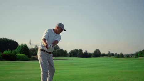 senior golf player practicing hitting ball on grass field. man training outdoors