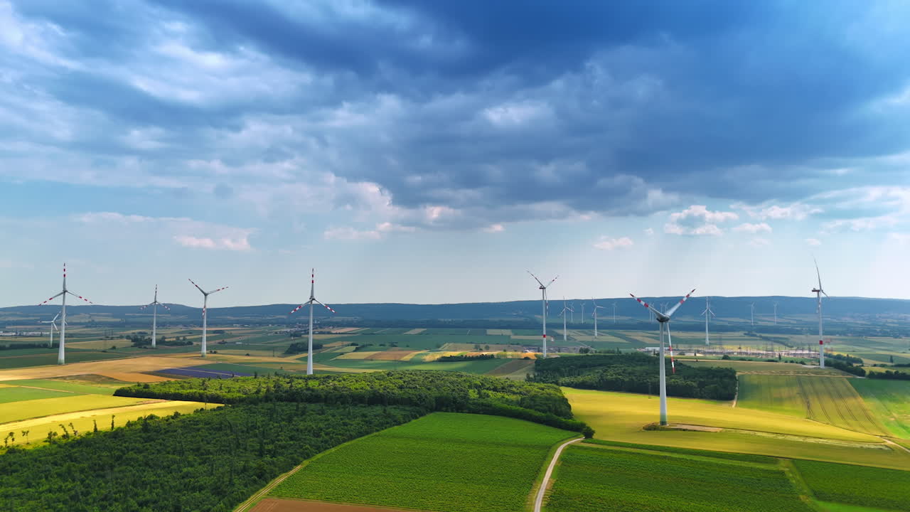 Picturesque fields with modern wind mills producing sustainable energy. Dark cloudscape covering the sky above