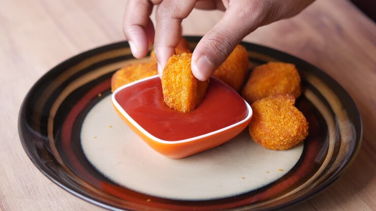 Hand Dipping Crispy Chicken Nuggets in Tomato Sauce