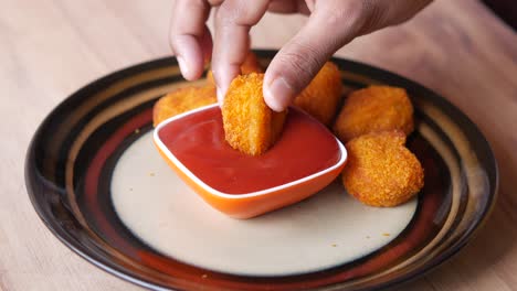 hand dipping crispy chicken nuggets in tomato sauce