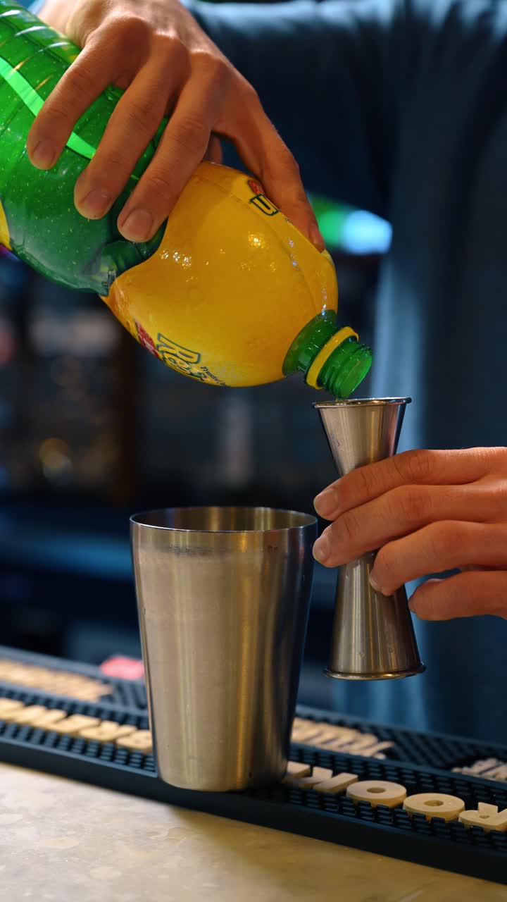 New York, USA, 15 aprile 2026: Versando succo di agrumi da una bottiglia gialla in un misurino di metallo. Misurando il succo di limone come ingrediente per la preparazione di cocktail su un bancone da bar professionale