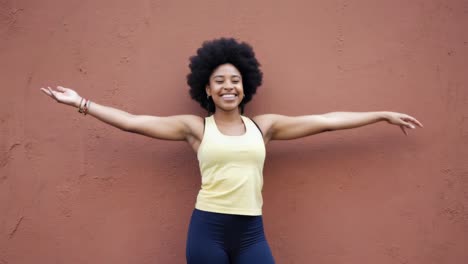 woman stretching in wellness concept, radiating confidence with open arms and bright smile against minimalist brown background, embodying contemporary fitness lifestyle and personal empowerment