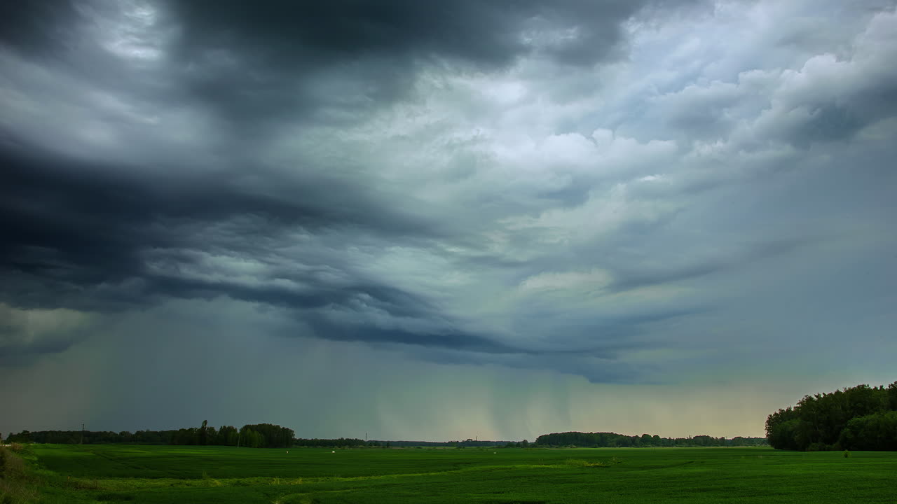 봄 저녁 멀리 숲이 보이는 푸른 들판 위로 검은 폭풍우가 몰아치는 비구름의 타임랩스 비디오