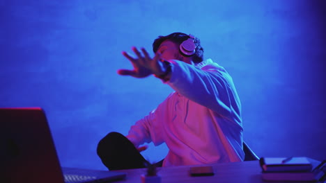 happy young man dancing and listening to music with wireless headphones on a colorful neon light background