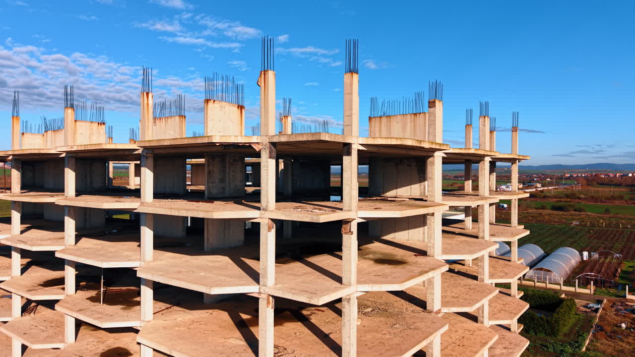Distancing from the cement carcass of the multi-storied building under construction. Hot-houses and residential houses at backdrop