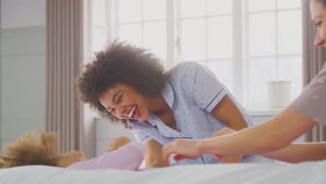 familia con dos madres con pijama jugando en la cama en casa con su hija