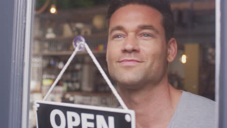 propietario masculino de una pequeña empresa girando un letrero abierto en una tienda o cafetería