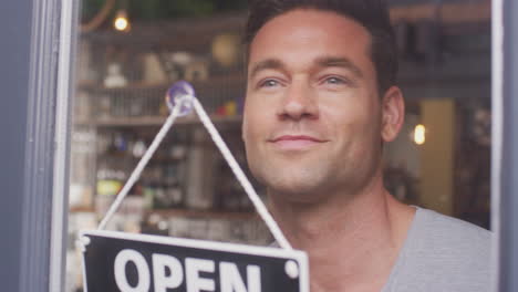 male owner of small business turning round open sign in shop or cafe