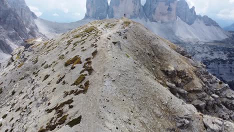 una vista increíble de un hombre parado solo en una formación rocosa con vista a tre cime di lavaredo con nubes en el fondo