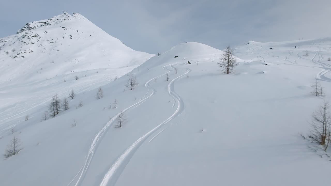 FPV drone flies towards ski tourer raising poles in celebration on snowy mountain peak, revealing ski tracks in fresh powder, Cheneil, Aosta Valley, Italy. Winter sport
