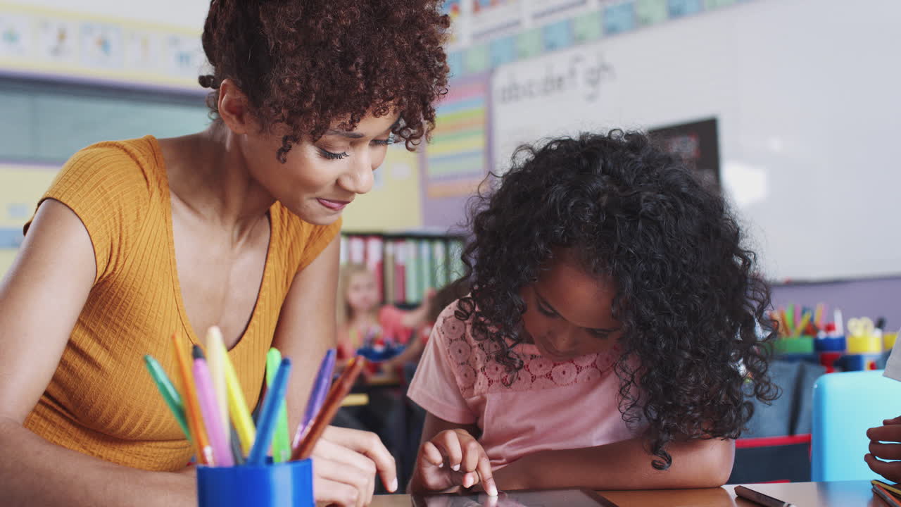 maestra de escuela primaria y alumna dibujando usando tableta digital en el aula