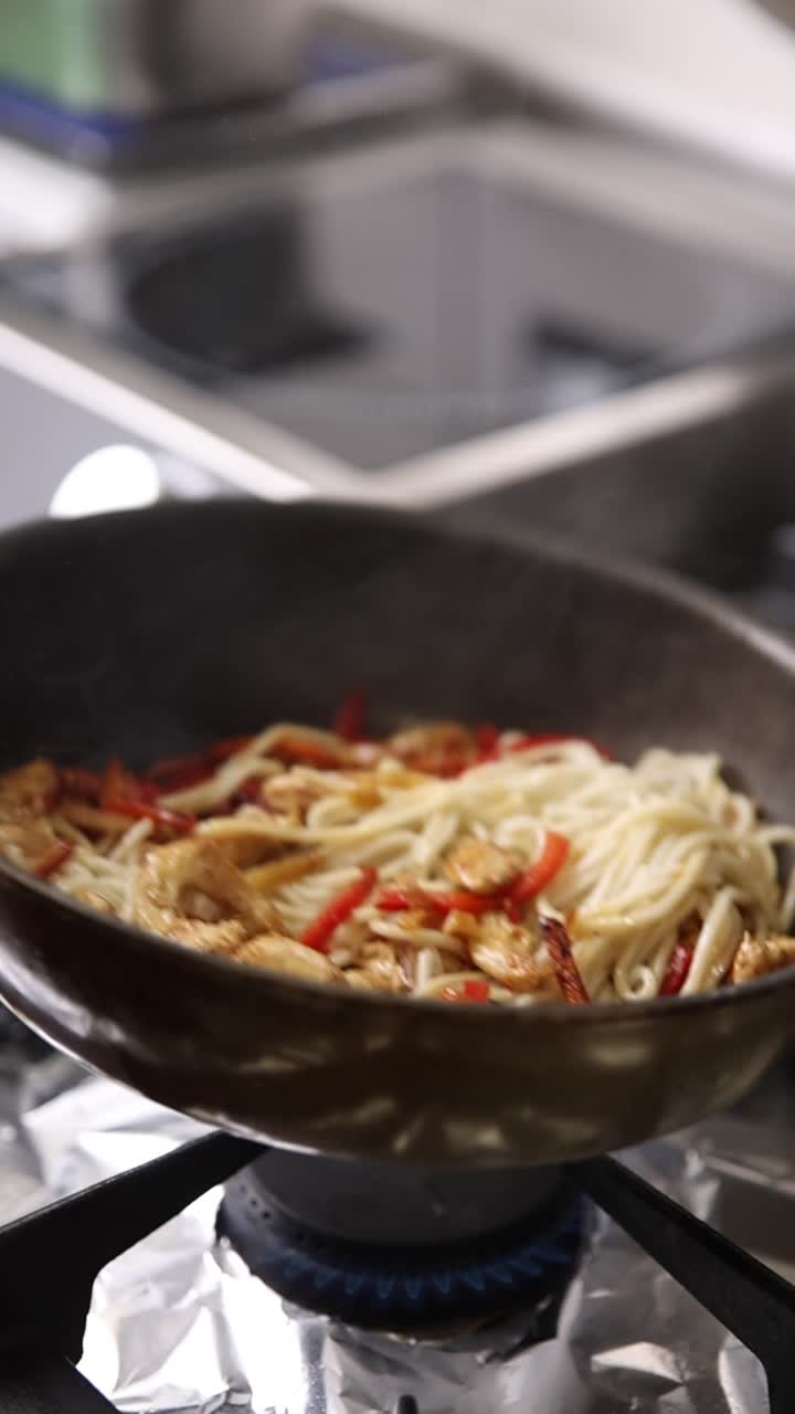 Wokstegning af nudler med kylling og peberfrugter i en wok