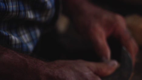 close up of country man's hands working with wood in his old workroom on a wooden workplace at night with a smooth warm light