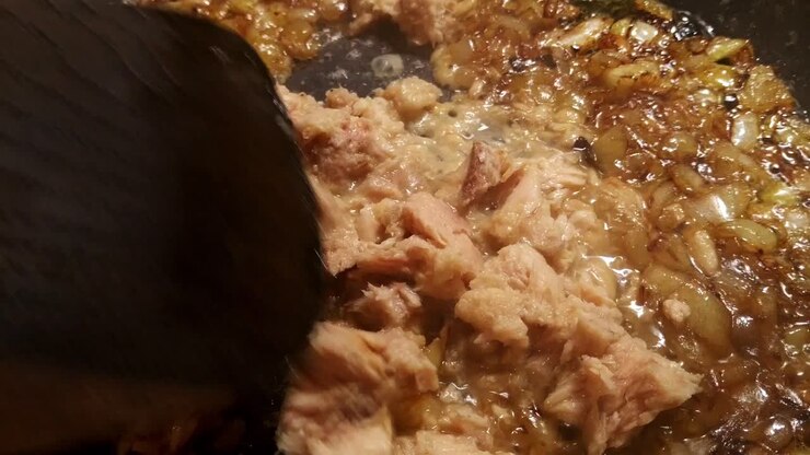 Close up of tuna fish frying in a black frying pan with white onions that have turned golden brown