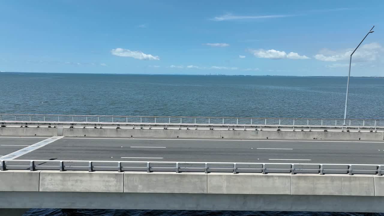 테드 스무트 메모리얼 브릿지 (ted smoot memorial bridge) 의 트래킹 에 드론이 있습니다. 모레톤 베이 (moreton bay) 의 물 위에 있는 카메라와 배경으로 열린 바다, 고 은 날의 한낮에 찍은 사진입니다.