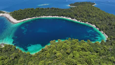 deep blue saltwater lake with turquoise shallows on mljet island, aerial orbit