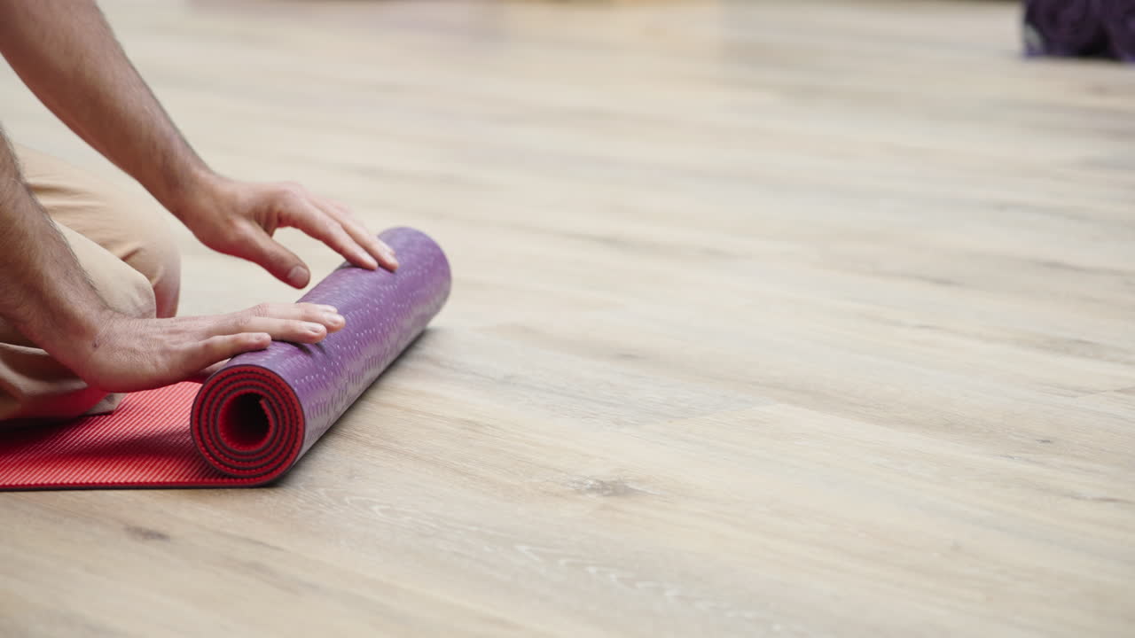 Manos enrollando una colchoneta de yoga en un suelo de madera.