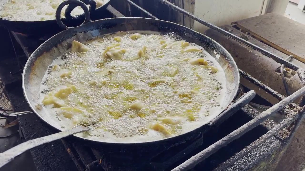 Closeup view of samosas deep frying in bubbling hot oil inside a large iron kadai in a traditional Indian kitchen!