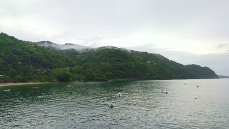 Drone-over-ocean-with-boats,-birds-flying-and-montain