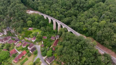 A-viaduct-with-a-small-steam-train-at-the-edge-of-the-cliff-moves-slowly-forward,-carrying-tourists-to-the-station-at-Martel-in-the-Lot-region-of-France